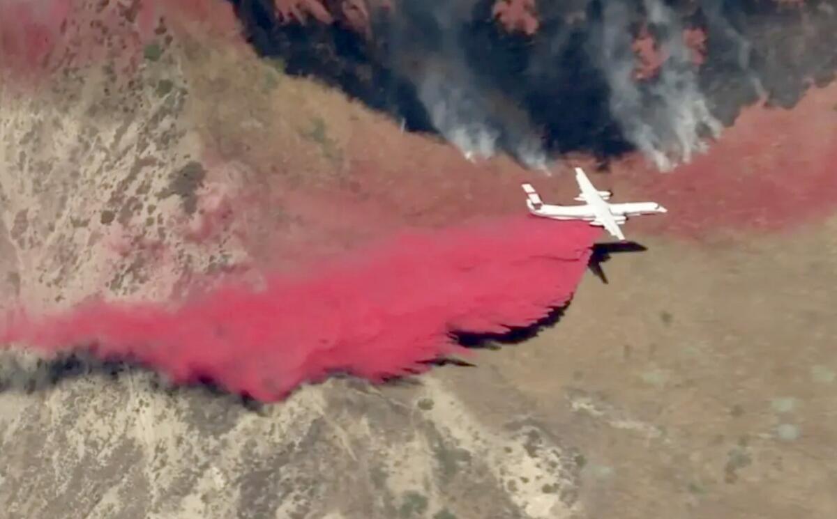 An airplane drops a red-pink substance on a hillside.